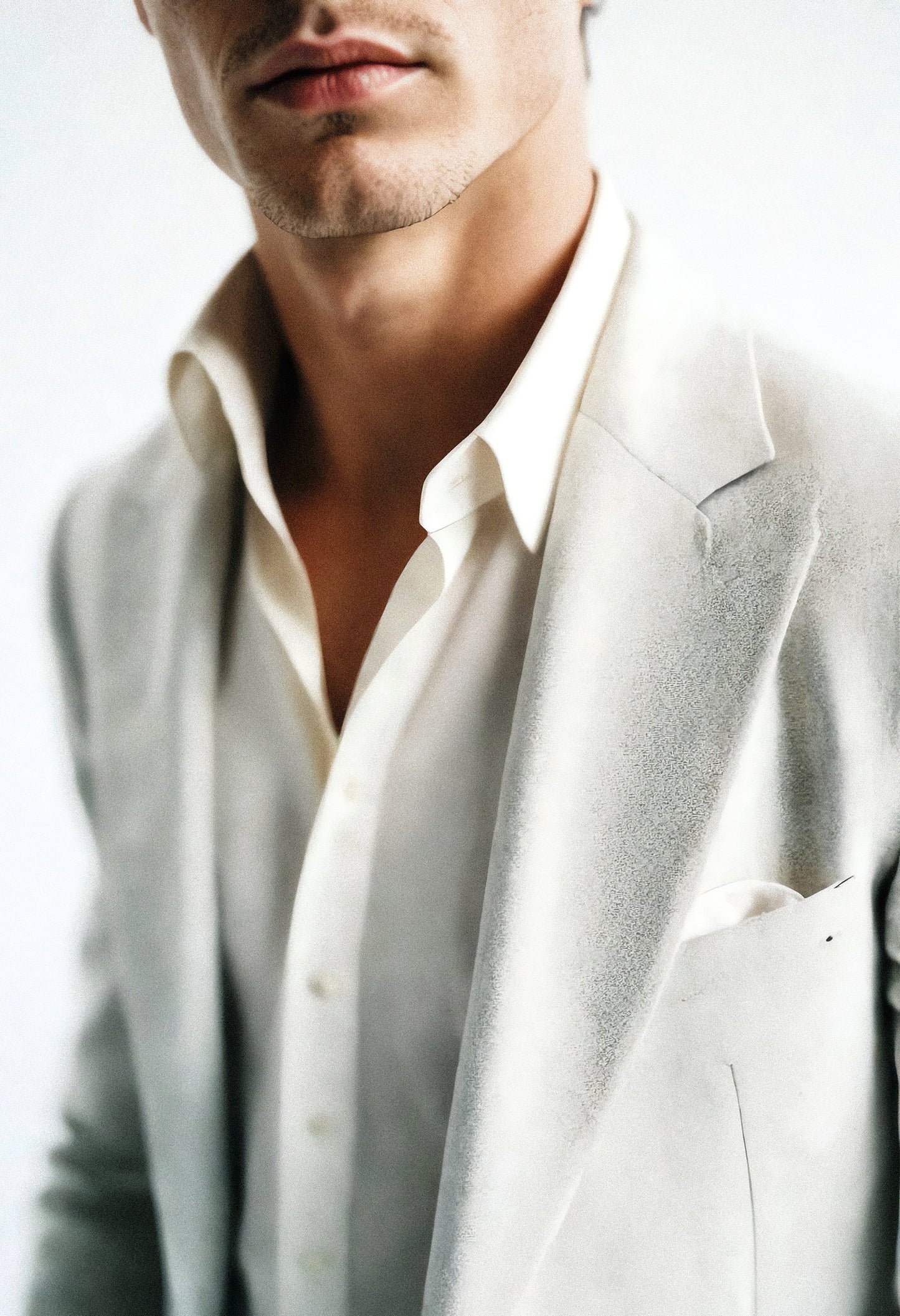 A man dressed in a tailored white suit with a crisp shirt, showcasing modern fashion and elegance in a minimalist setting