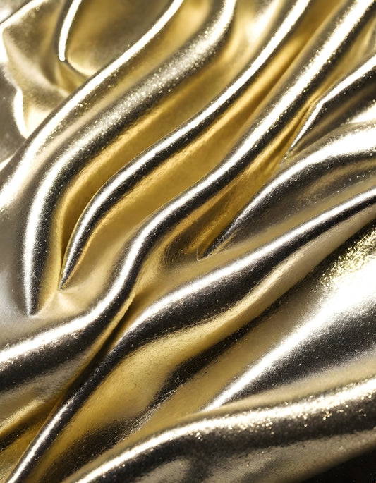 Metallic golden and silver fabric creates elegant textures with intricate folds and reflections under soft lighting