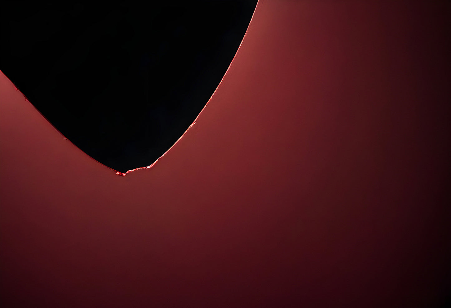 A close-up view of a droplet suspended from the edge of a dark object with a red backdrop, creating an abstract and intriguing visual