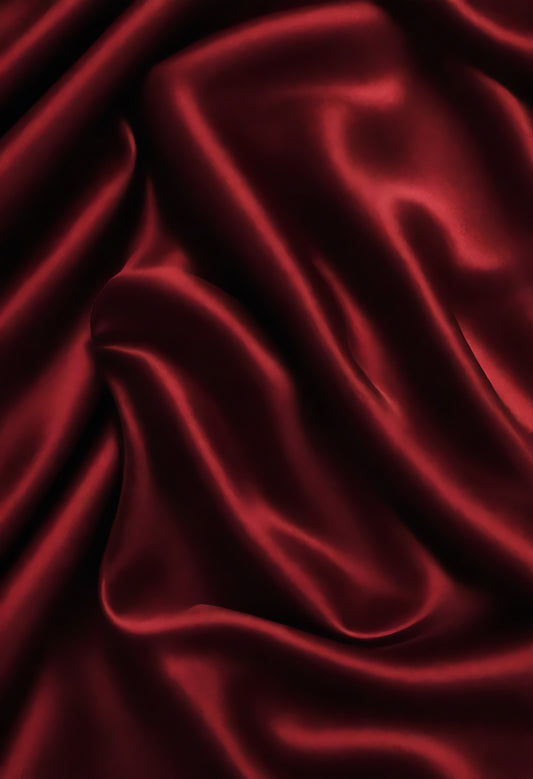 Elegant deep red satin fabric draped smoothly, showcasing soft folds and a rich texture under natural light