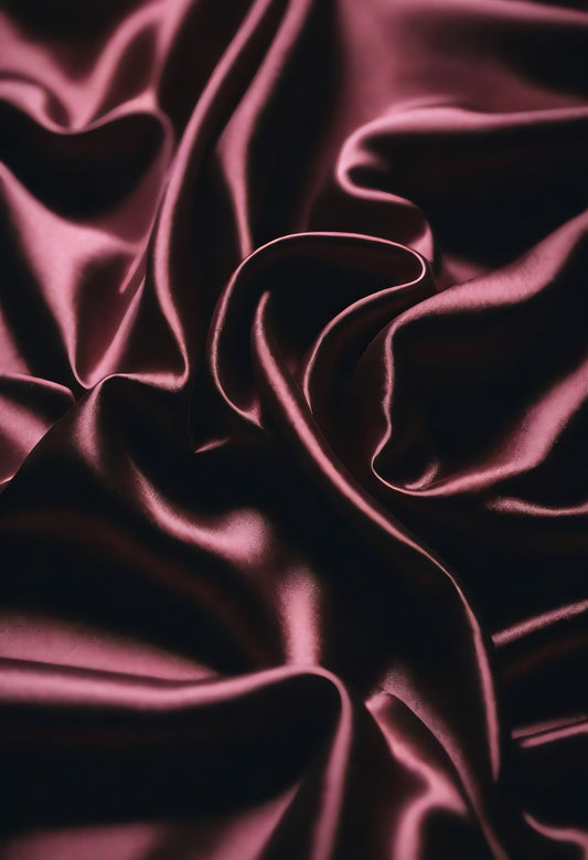 Smooth burgundy fabric creates an elegant texture, draped artfully on a surface in soft, natural light to highlight its sheen