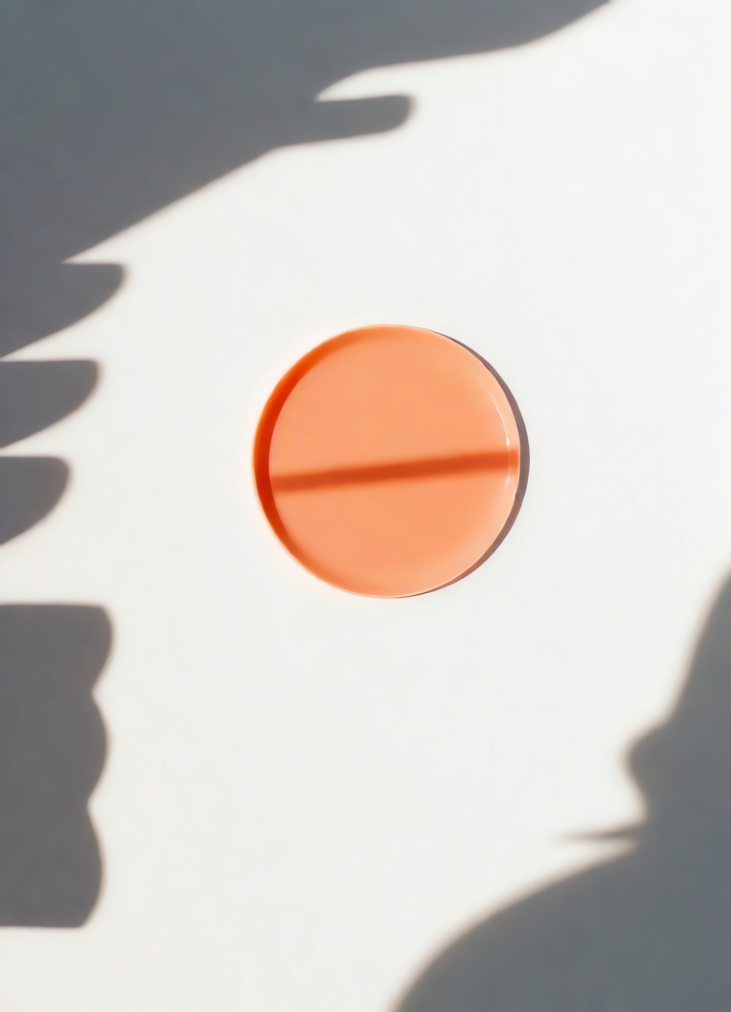 Circular orange object on white surface with shadow patterns in bright natural light