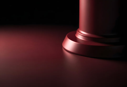 A close-up view of a polished red column base on a smooth surface illuminated by soft light in a dim setting