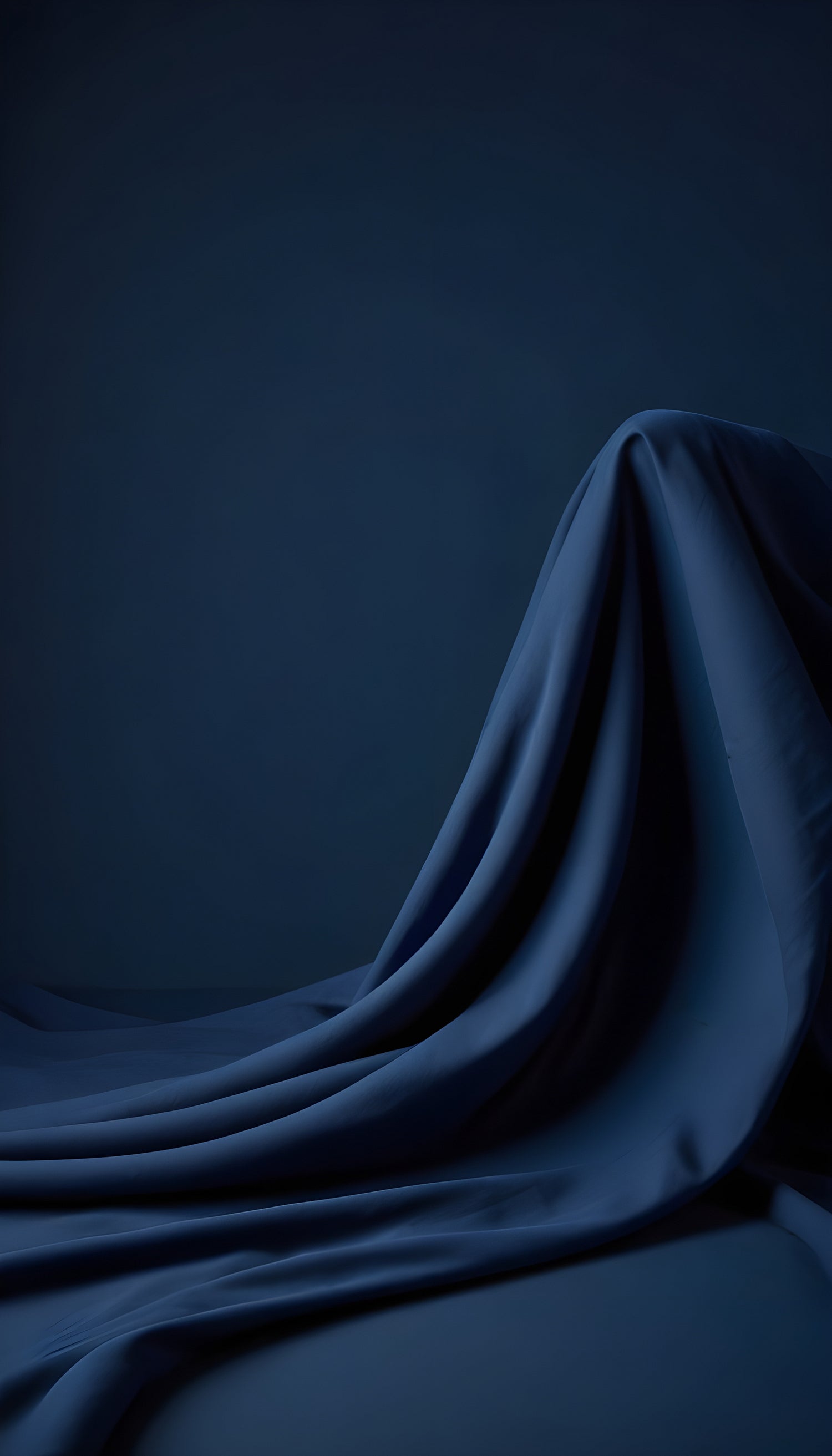 A dark blue fabric draped elegantly over a surface, creating soft waves and shadows in low light conditions