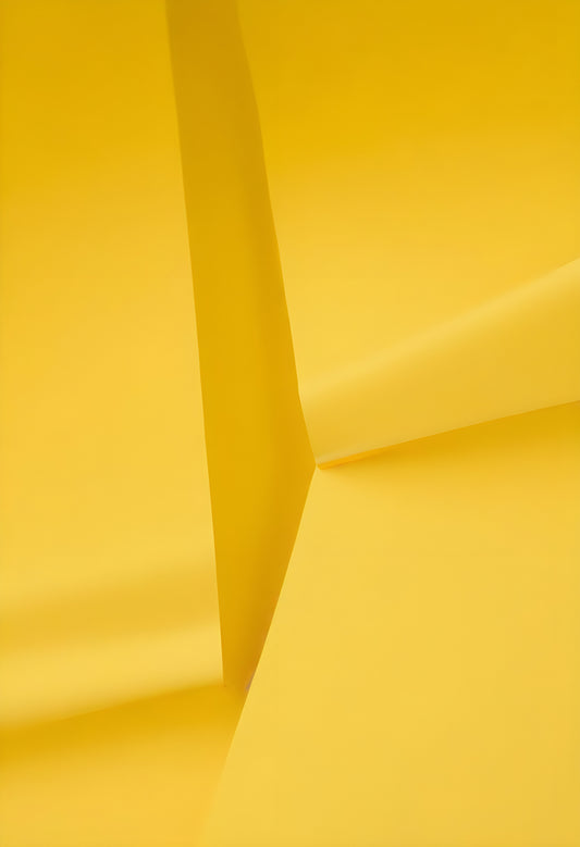 Bright yellow paper folds creating dynamic shapes and textures in a minimalist setting with soft lighting