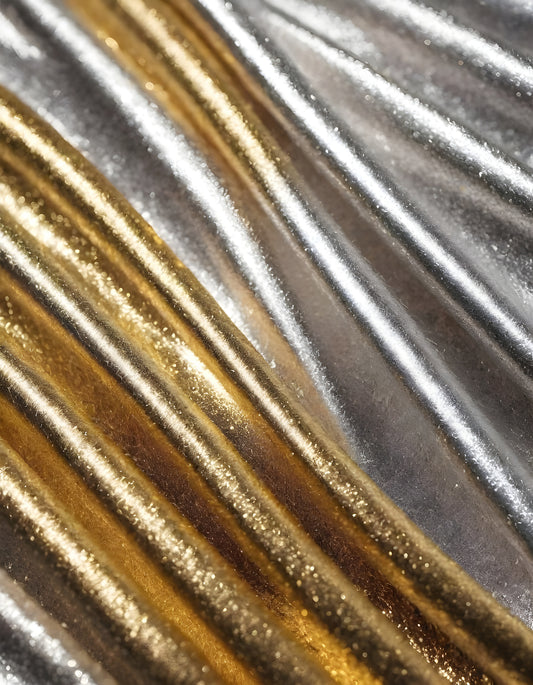 Shimmering gold and silver fabrics layered together in a luxurious arrangement during daylight