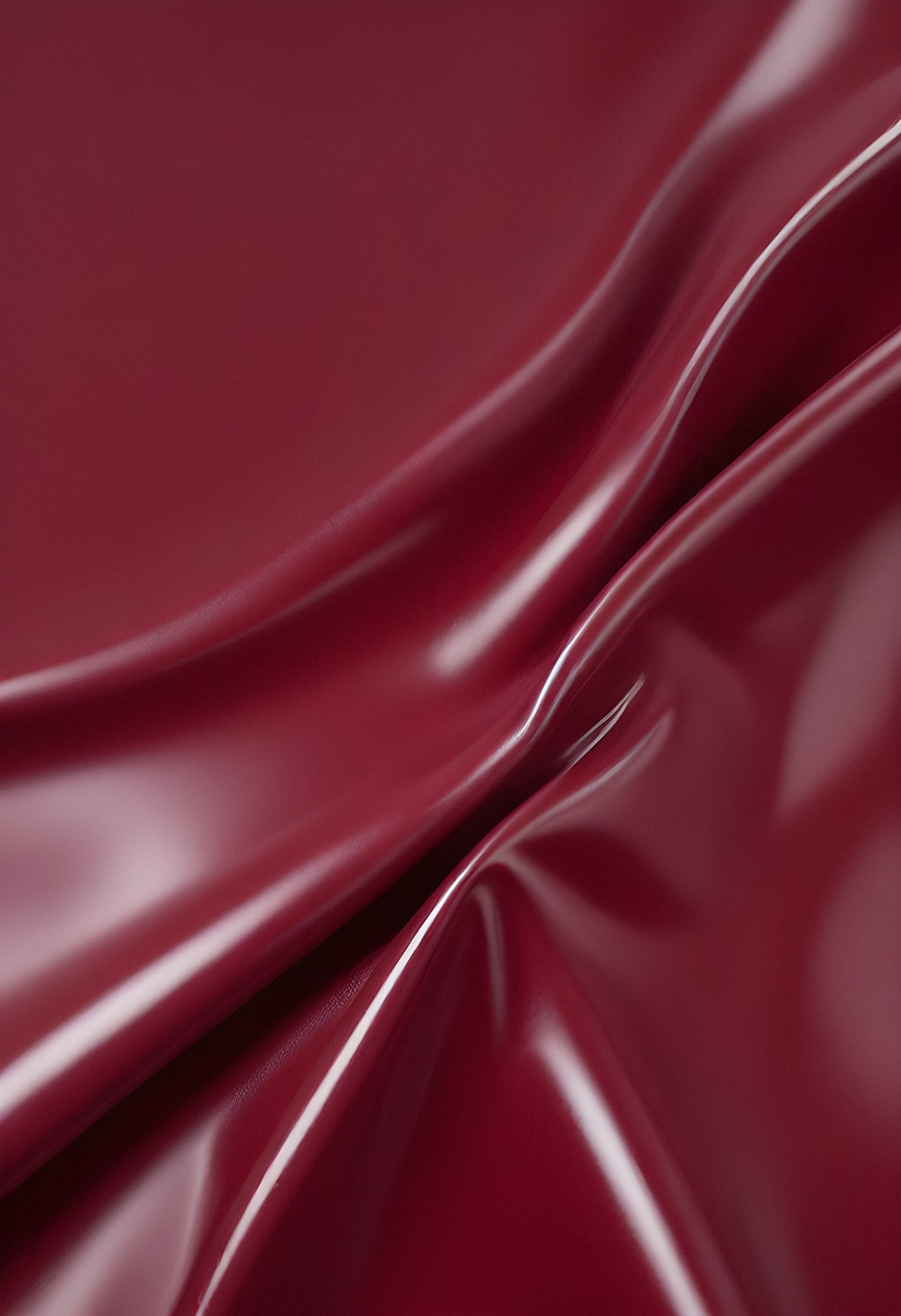 A close-up of deep red glossy leather fabric with soft, flowing folds illuminated by gentle light