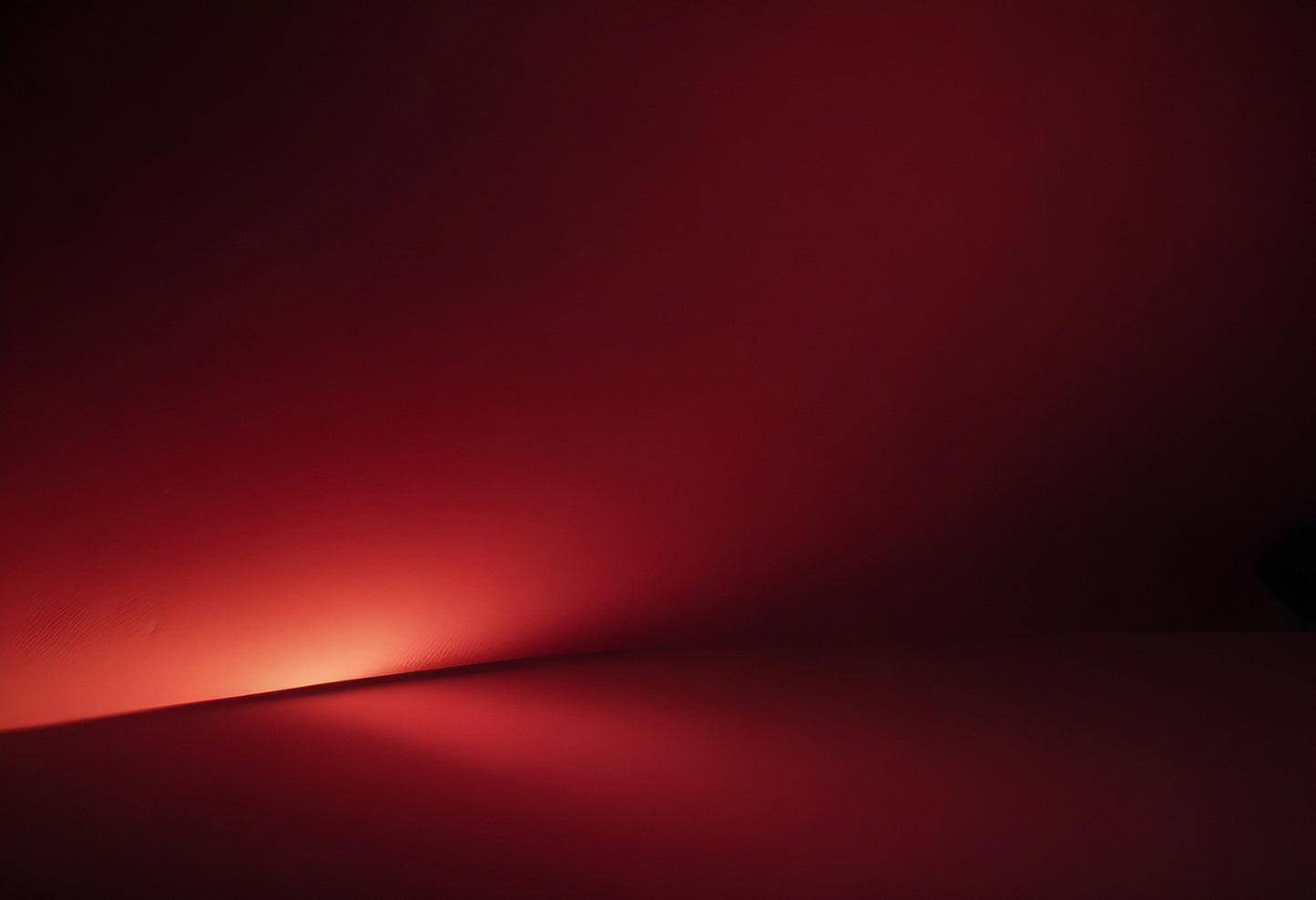 A soft red glow illuminates a smooth surface, creating an abstract display of light and shadow in a minimalistic setting