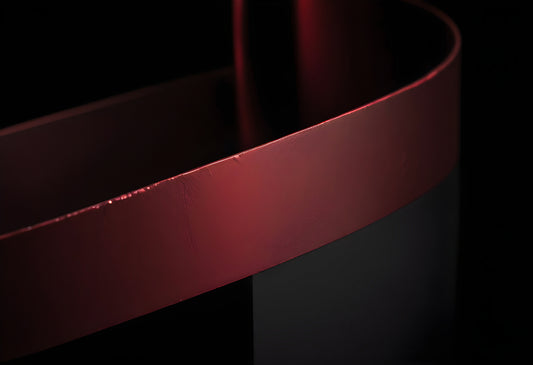 Close-up of a curved metallic surface reflecting red light against a black background in an abstract artistic setting