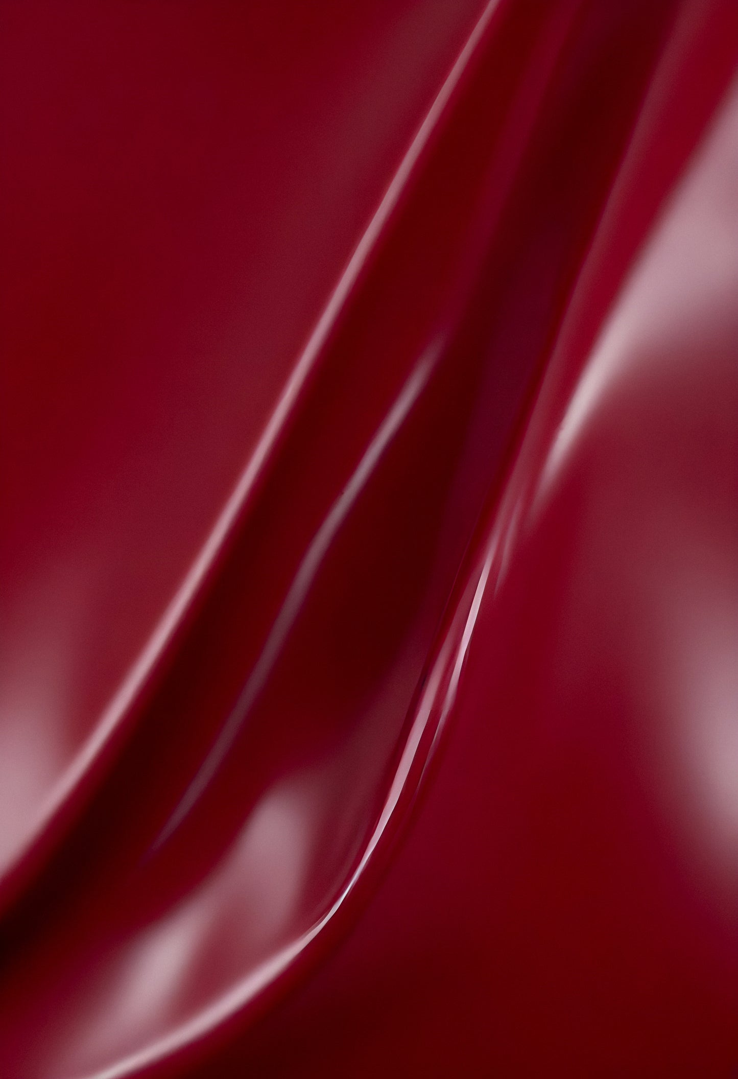 A close-up of deep red glossy leather fabric with soft, flowing folds illuminated by gentle light