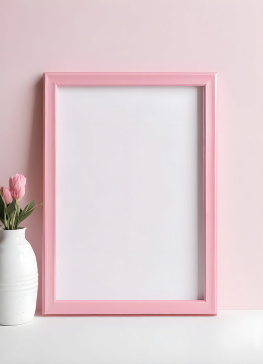 A minimalist pink frame on a soft pink wall, empty for art or a photo, paired with a white vase of pink flowers