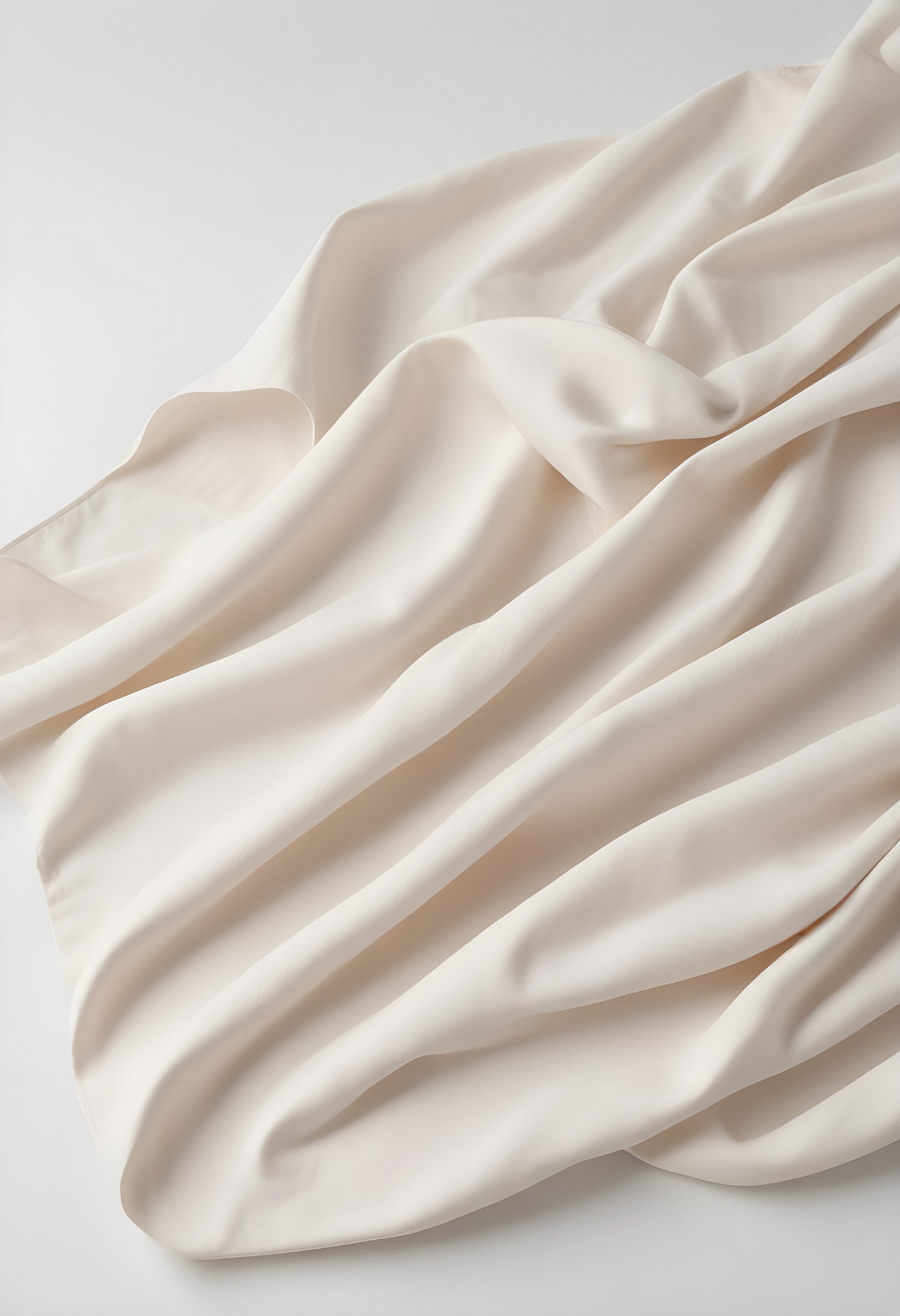 A soft cream fabric draped elegantly on a white surface, highlighting its smooth texture and graceful folds in natural light