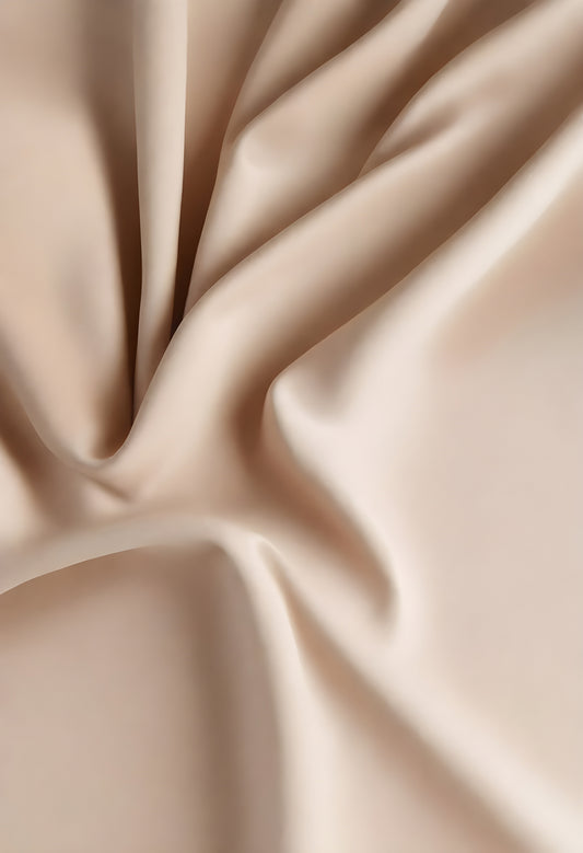 Elegant beige fabric draped gracefully on a surface, showcasing smooth texture and gentle folds in soft lighting