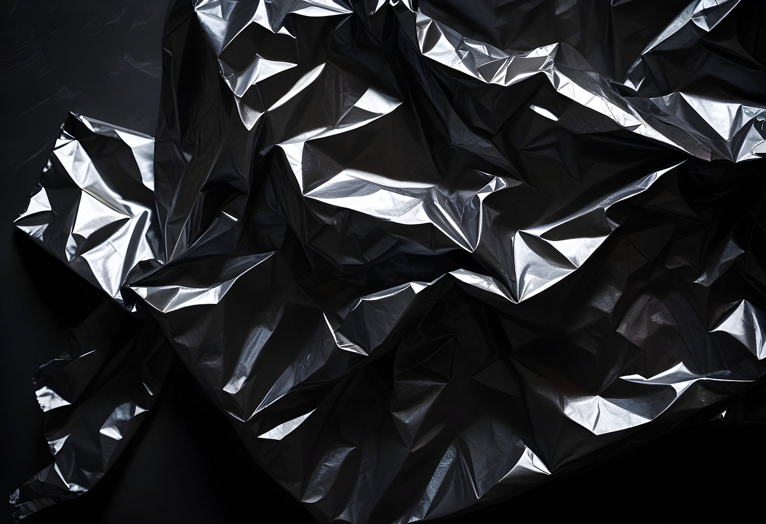 Crumpled black plastic sheet on a dark surface showcasing texture and light reflections