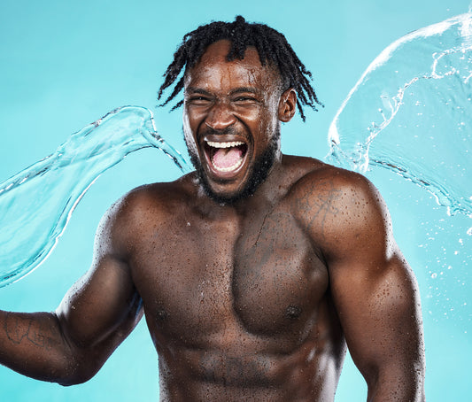 A muscular man joyfully splashes water in a vibrant blue studio environment during a dynamic fitness photoshoot