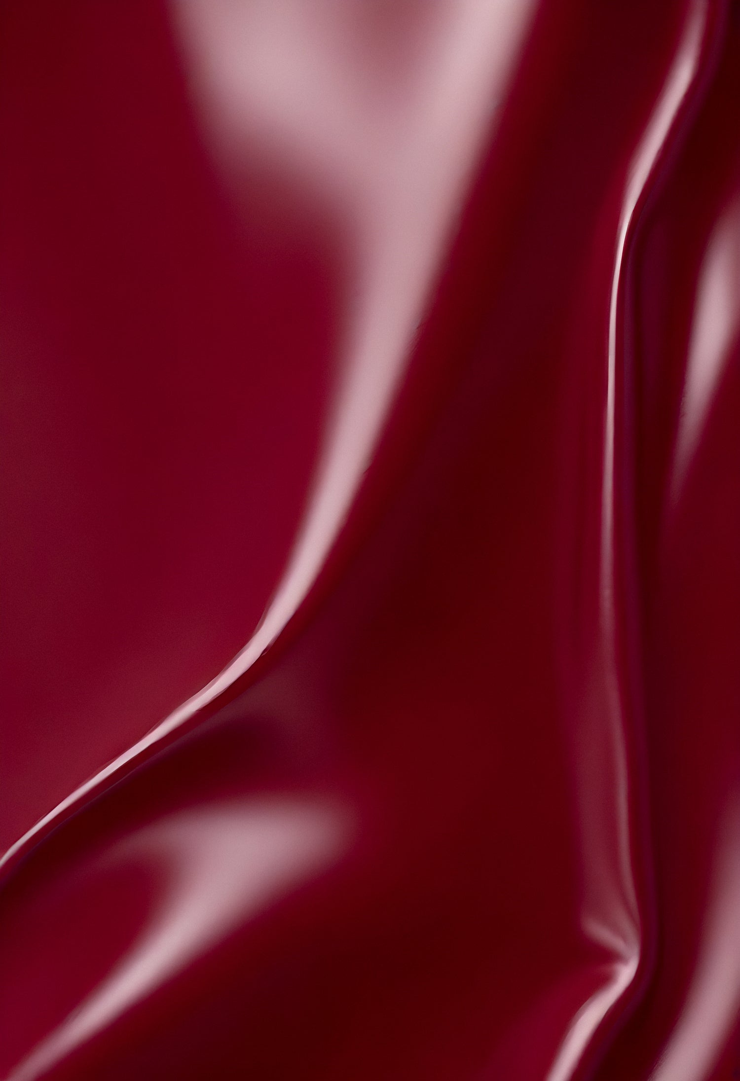 A close-up of deep red glossy leather fabric with soft, flowing folds illuminated by gentle light