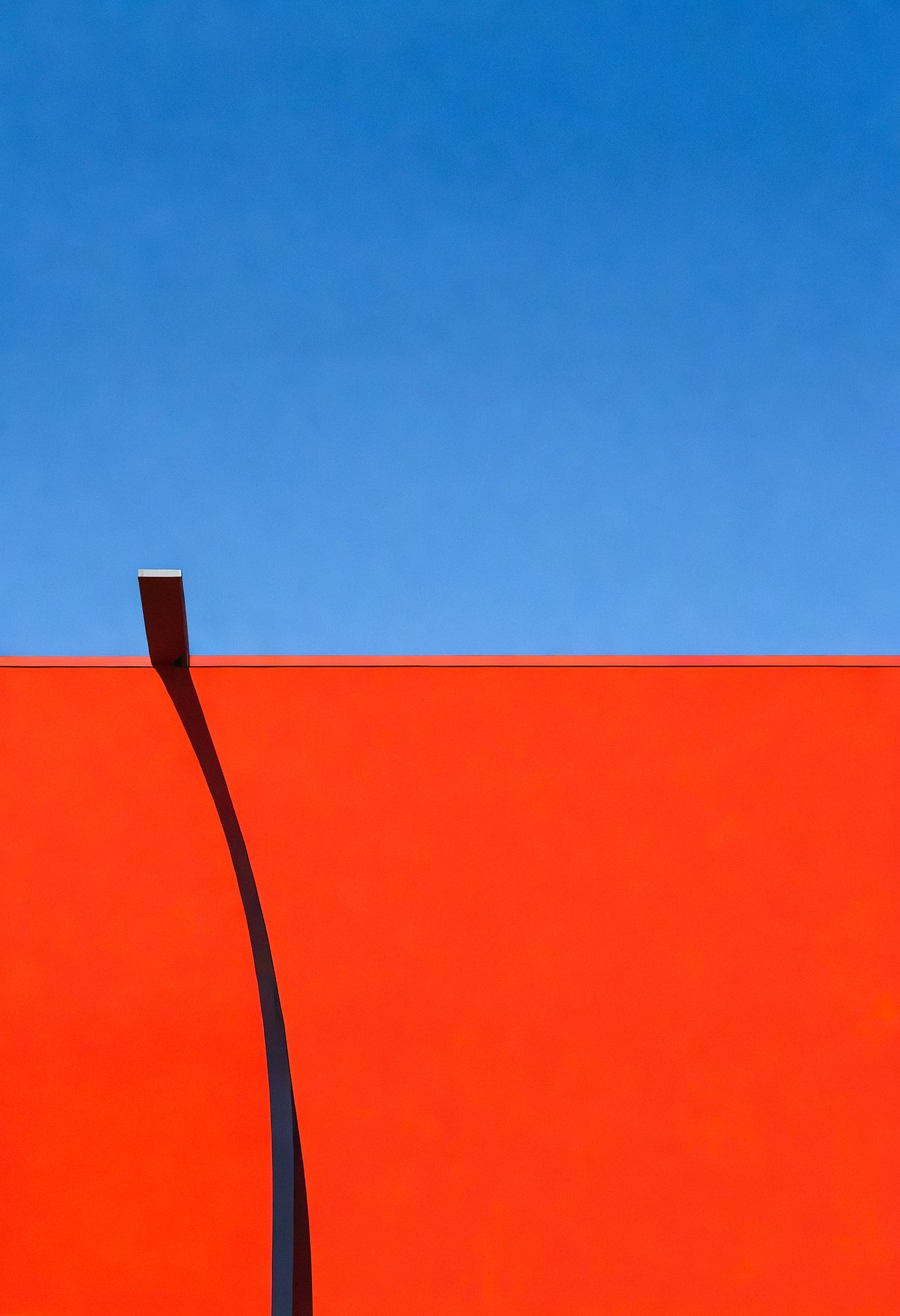 Vivid red wall contrast against bright blue sky highlighting simplicity and modern architecture in a minimalist setting