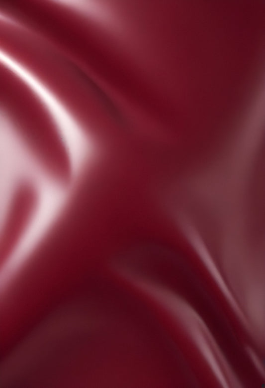 A close-up of deep red glossy leather fabric with soft, flowing folds illuminated by gentle light