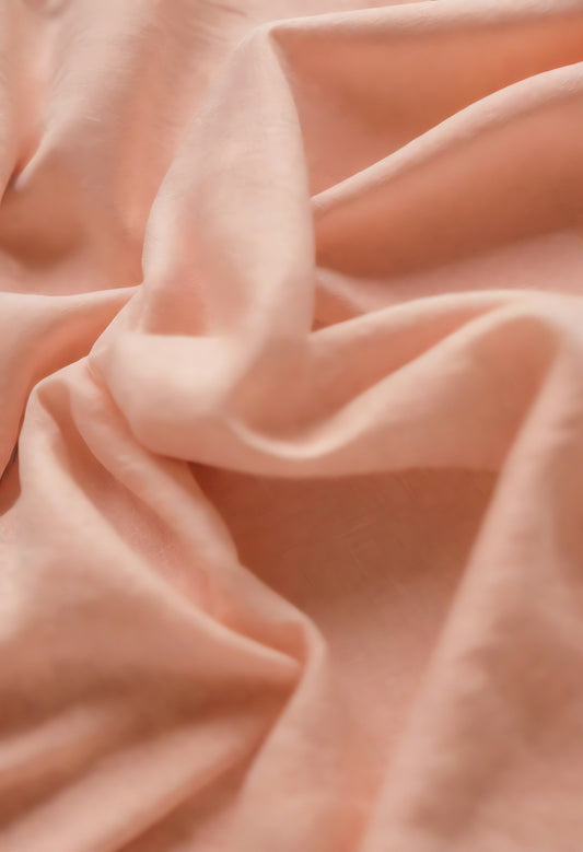 Soft peach fabric draped elegantly on a neutral background during daylight