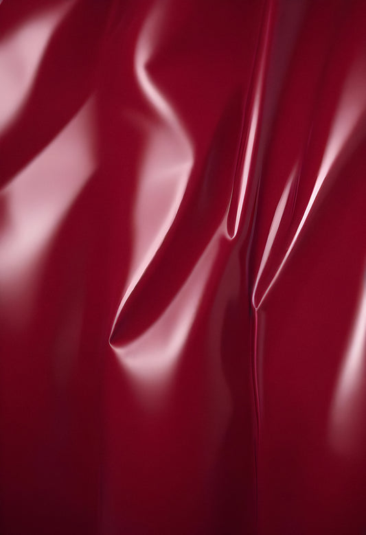 A close-up of deep red glossy leather fabric with soft, flowing folds illuminated by gentle light