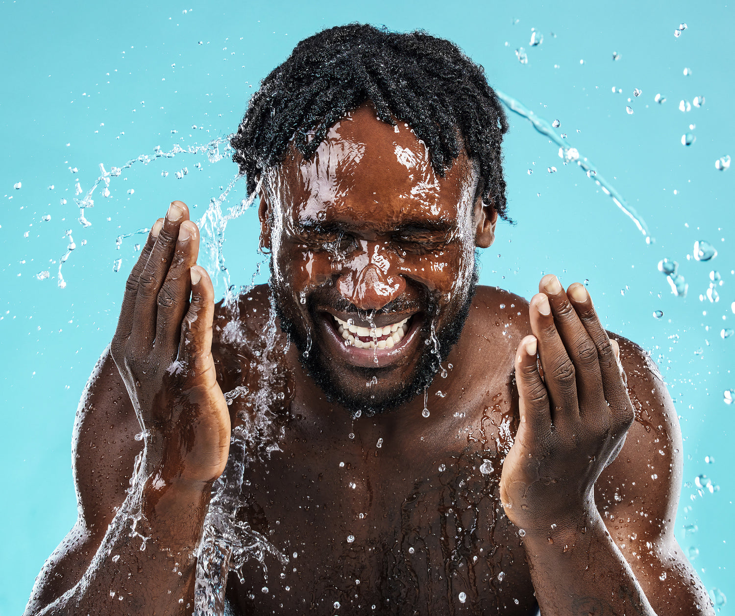 A man enjoying water splashes against a bright blue background during a playful summer moment in a studio setting