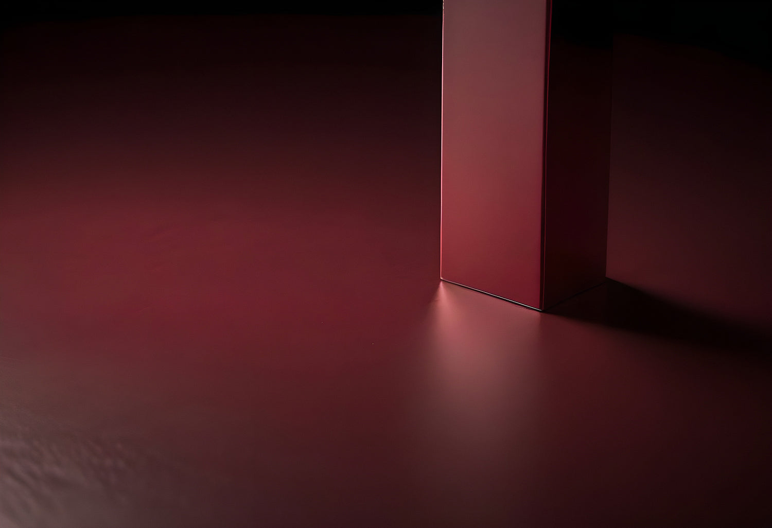 A minimalist red structure casting shadow on a smooth surface in a dimly lit environment during evening hours