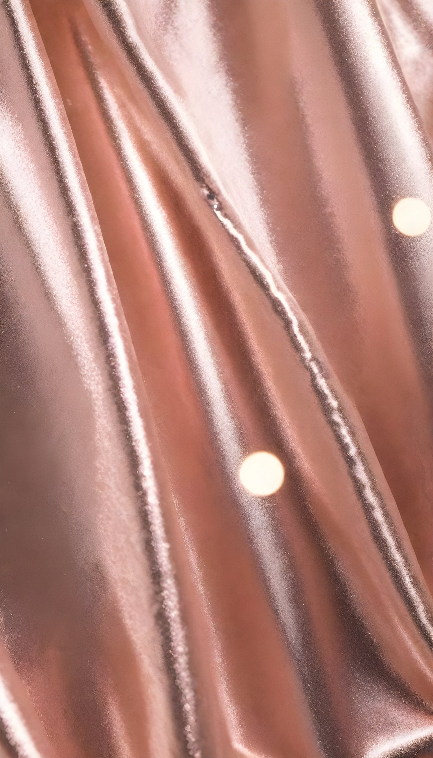 Shimmering rose gold fabric draping elegantly with soft folds under bright light in a studio setting