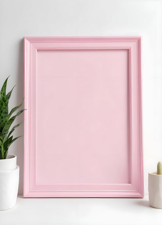 Empty pink picture frame rests against a soft background beside green plants in minimalist decor setup