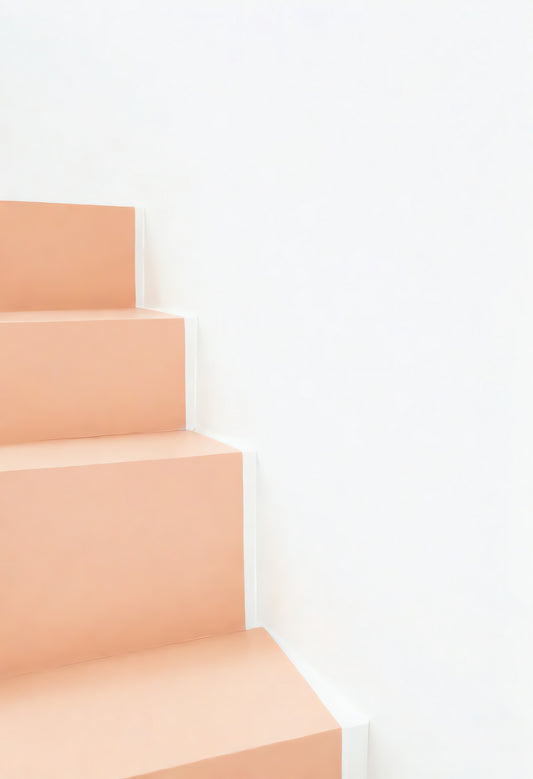 A close-up of soft peach-colored stairs leading upward against a bright white wall in a modern interior space during daylight