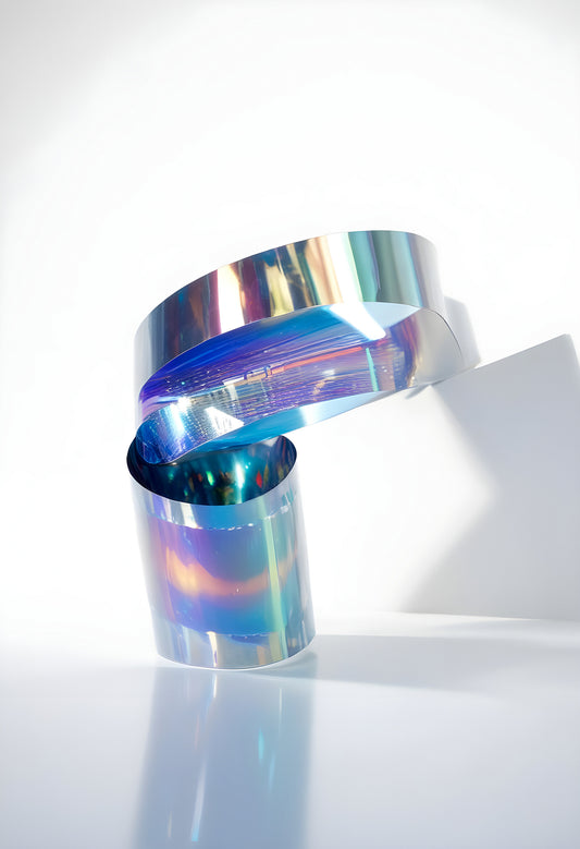 A shimmering, twisting ribbon of holographic film reflecting light in a minimalistic studio setting during the daytime