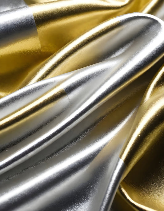 Metallic golden and silver fabric creates elegant textures with intricate folds and reflections under soft lighting