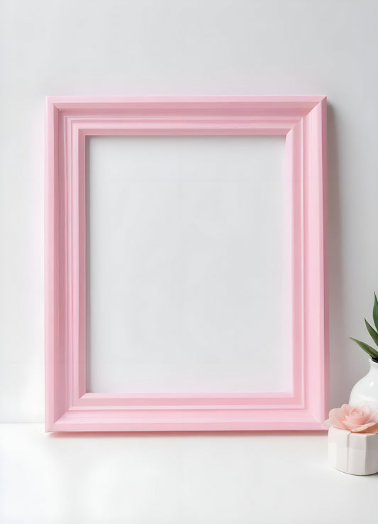 Empty pink frame resting on a white surface beside a vase with a single flower and a green plant