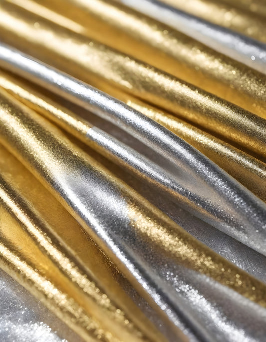 Metallic golden and silver fabric creates elegant textures with intricate folds and reflections under soft lighting