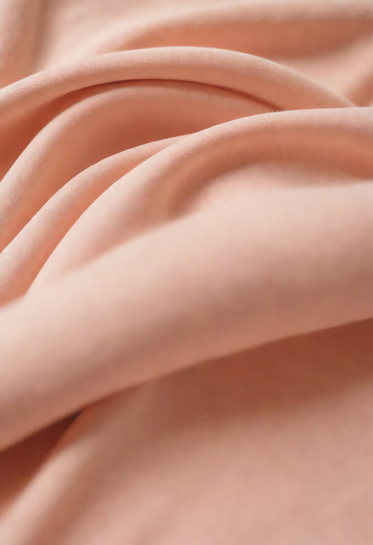 Soft peach fabric draped elegantly on a neutral background during daylight