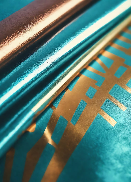 Shiny teal and gold foil rolls stacked together, reflecting light in a creative workspace