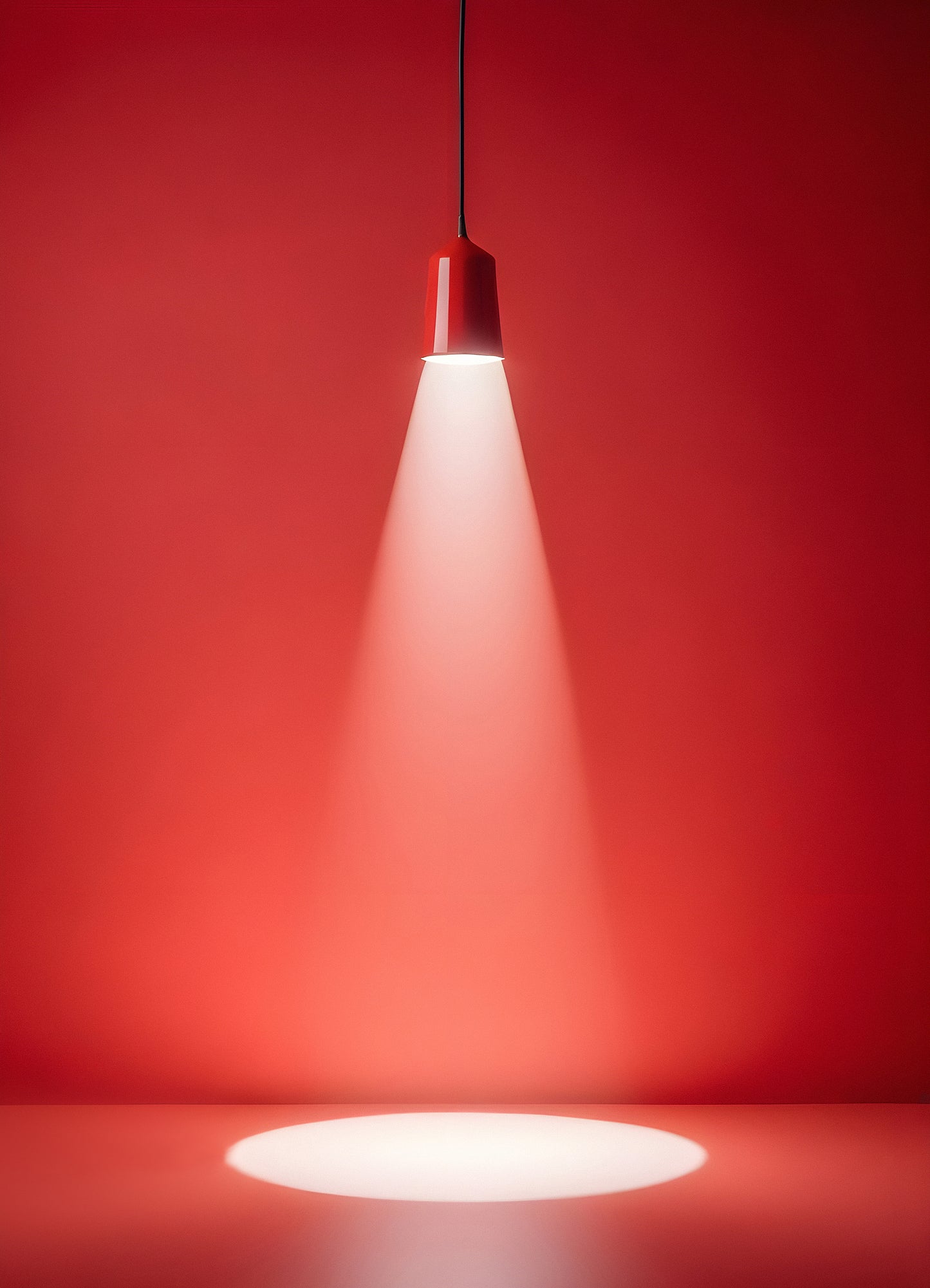 A red ceiling light casts a focused beam onto a smooth surface, creating an artistic effect in a minimalist setting