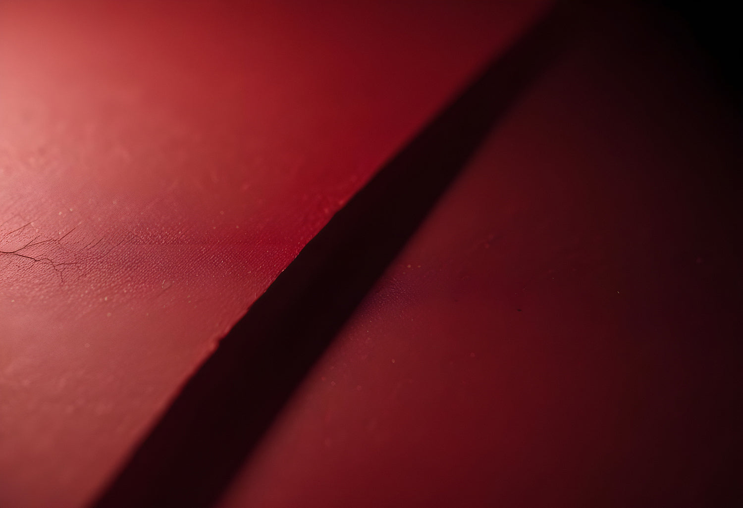 Close-up of a sharp object casting a shadow on a red surface with subtle textures in a dimly lit environment