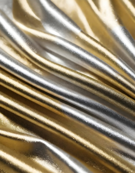 Metallic golden and silver fabric creates elegant textures with intricate folds and reflections under soft lighting