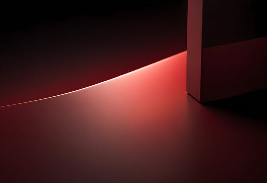 Soft red light illuminates a curved surface and geometric shape in a darkened space, creating a minimalist artistic effect