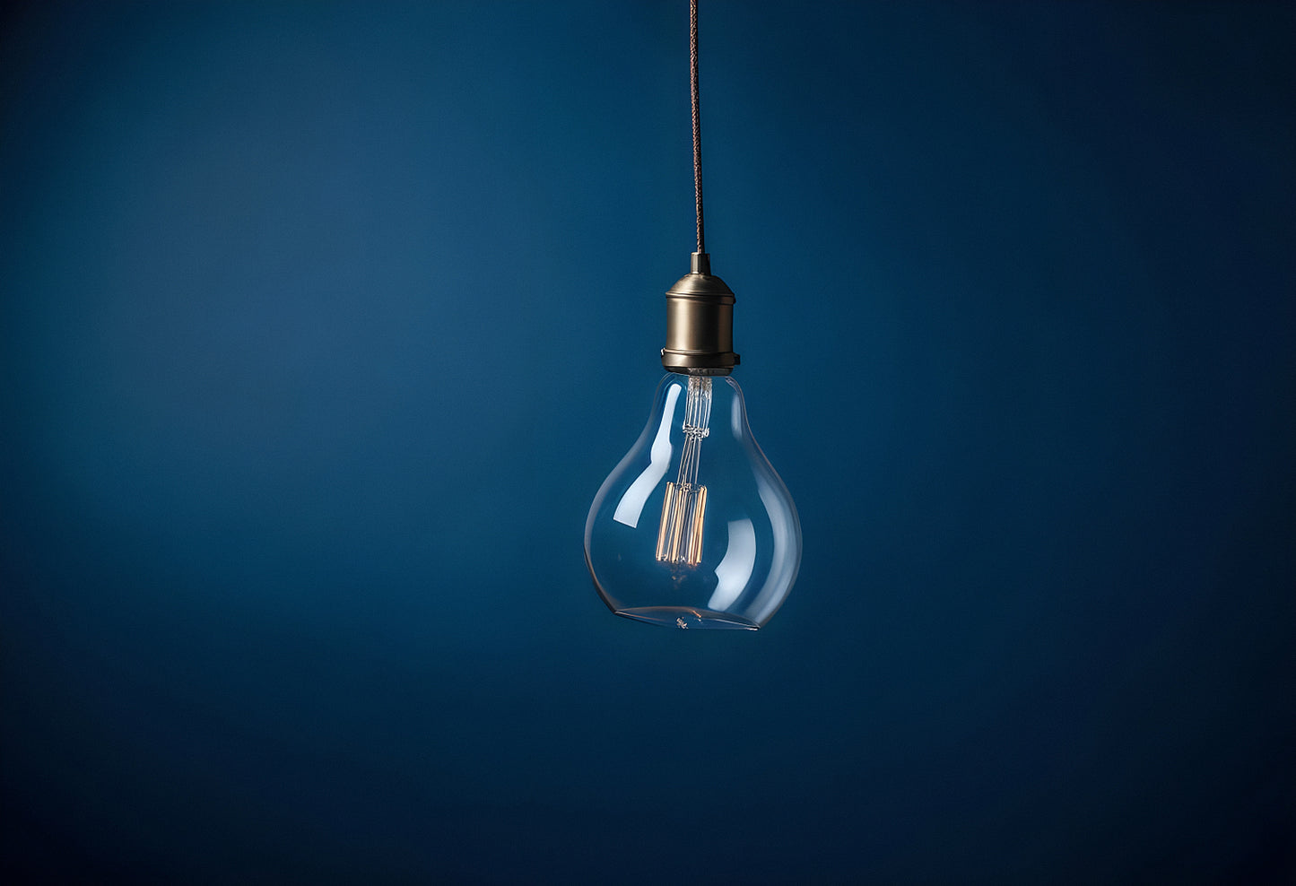 A vintage style hanging light bulb illuminated against a dark blue background creating an elegant and minimalist ambiance in the room