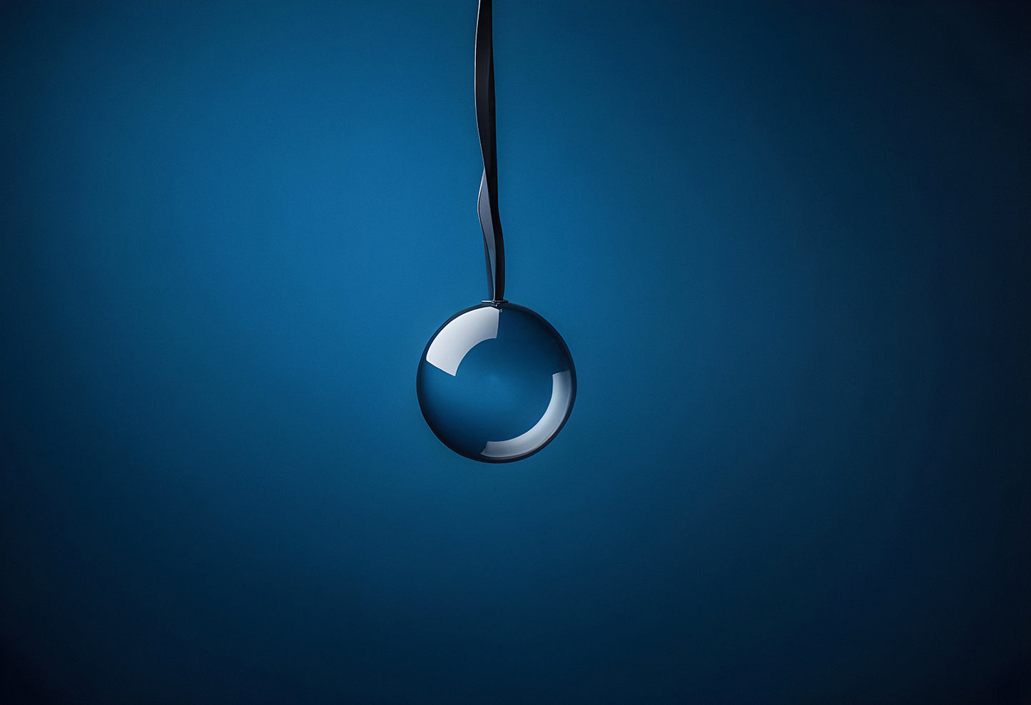 A glass ball suspended from a metal surface against a blue background