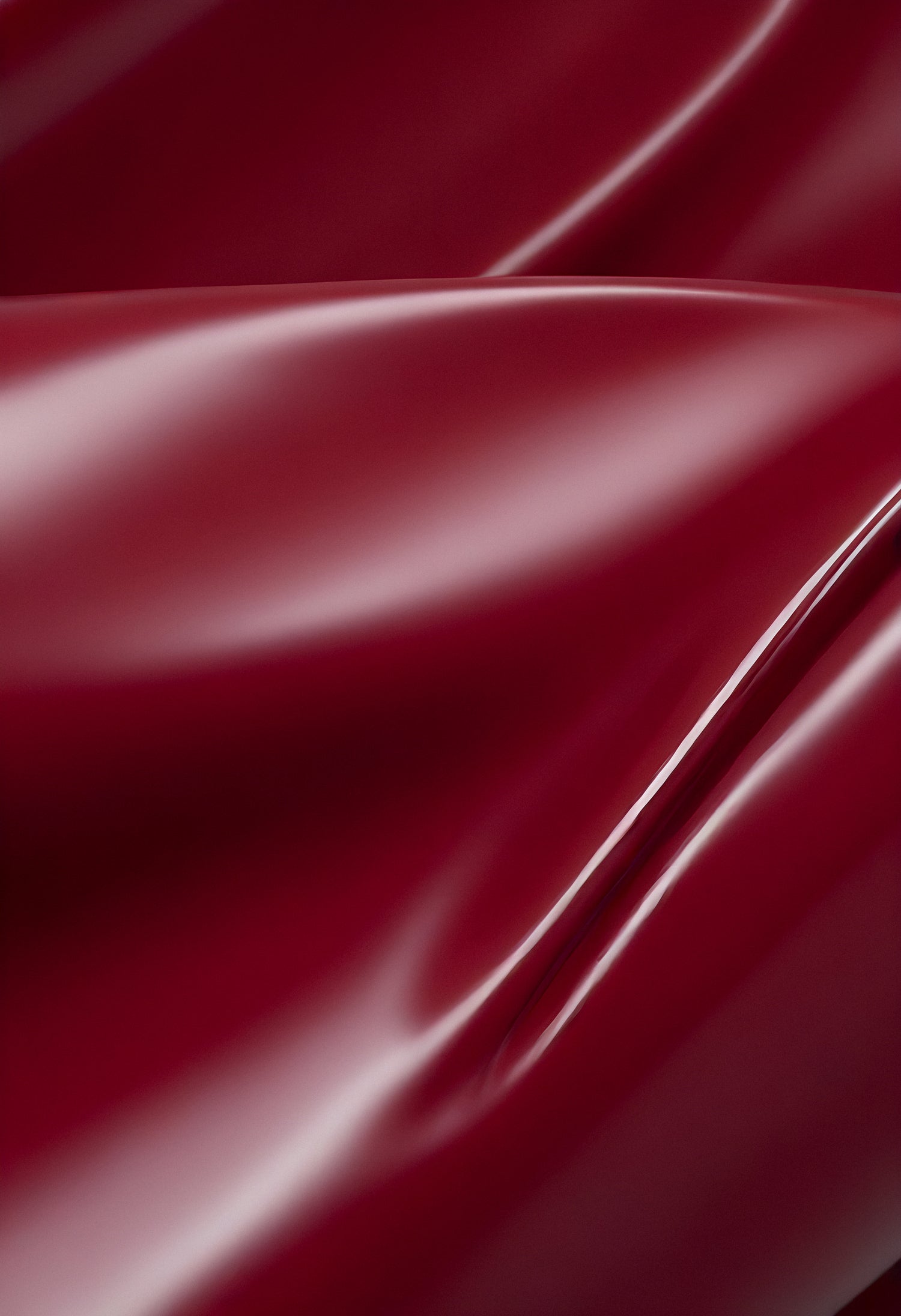 A close-up of deep red glossy leather fabric with soft, flowing folds illuminated by gentle light