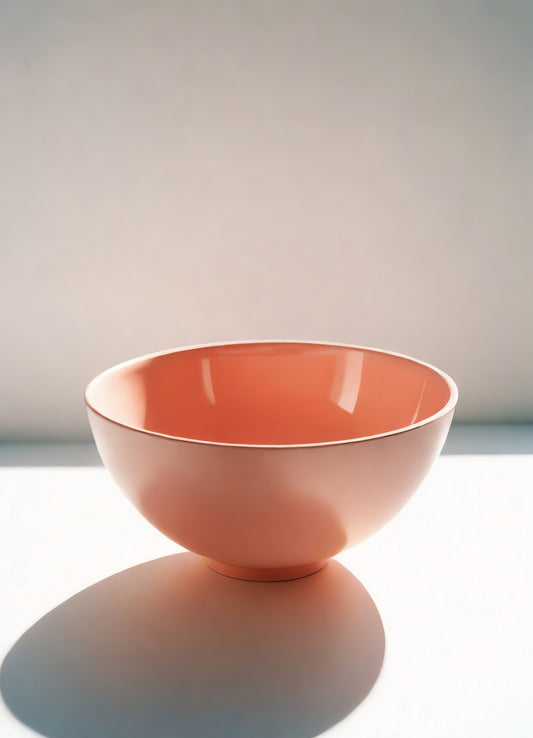 A simple, elegant pink bowl placed on a white surface with soft natural light illuminating its contours in a minimalist setting