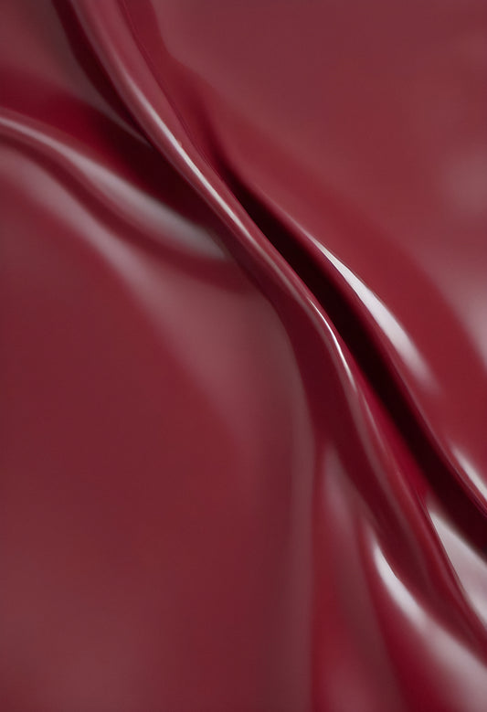 A close-up of deep red glossy leather fabric with soft, flowing folds illuminated by gentle light