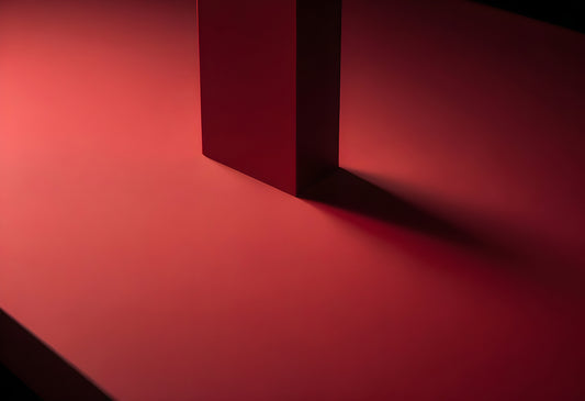 A minimalist red composition featuring a vertical block casting a shadow on a flat surface in dramatic lighting