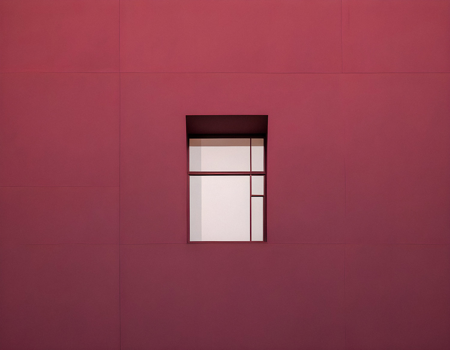 Minimalist architecture featuring a geometric window on a vibrant red wall during bright daylight