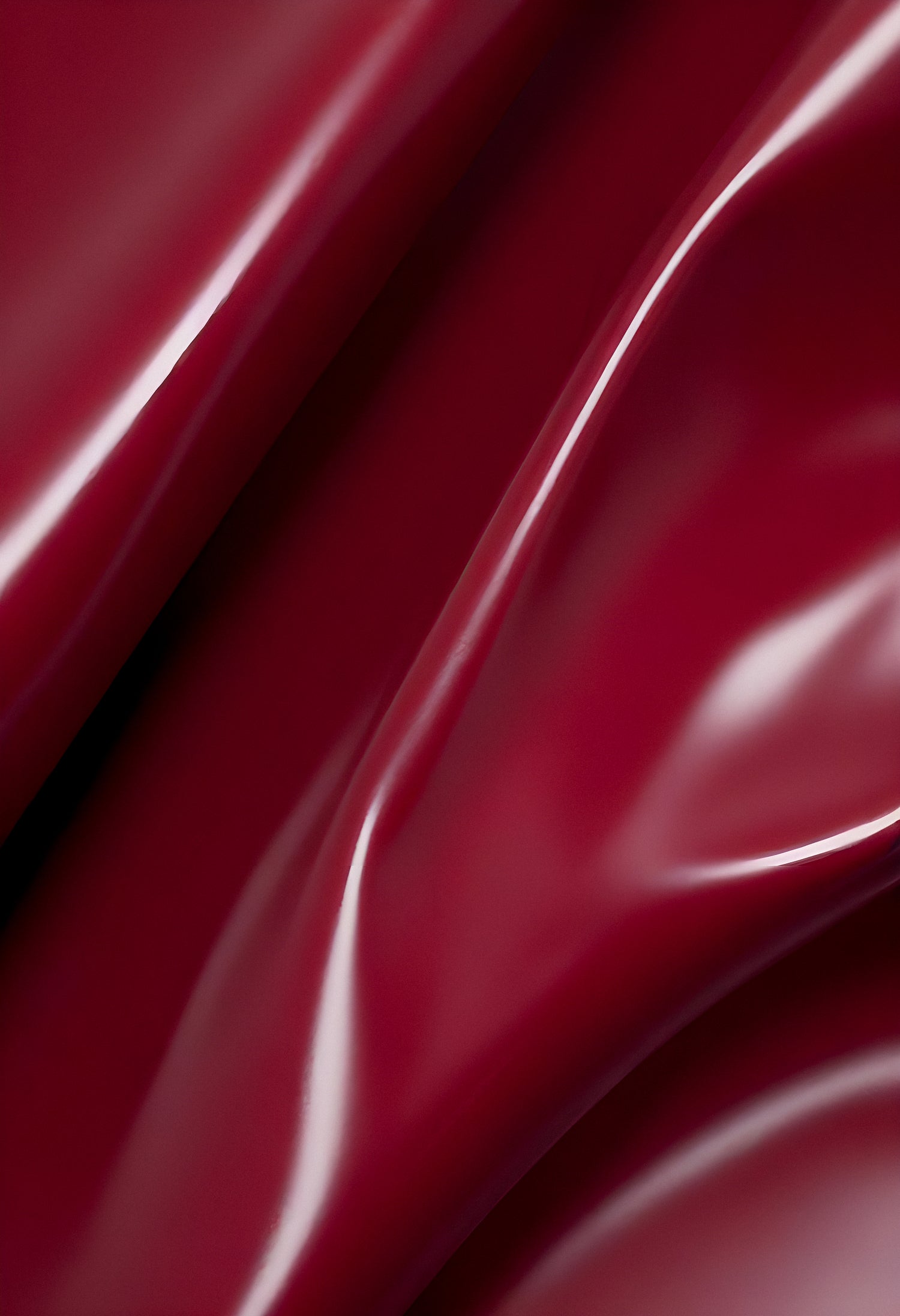 A close-up of deep red glossy leather fabric with soft, flowing folds illuminated by gentle light